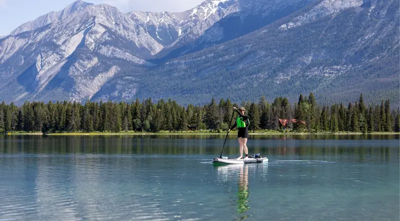 Paddleboarder on a calm Jasper National Park lake below the mountains
